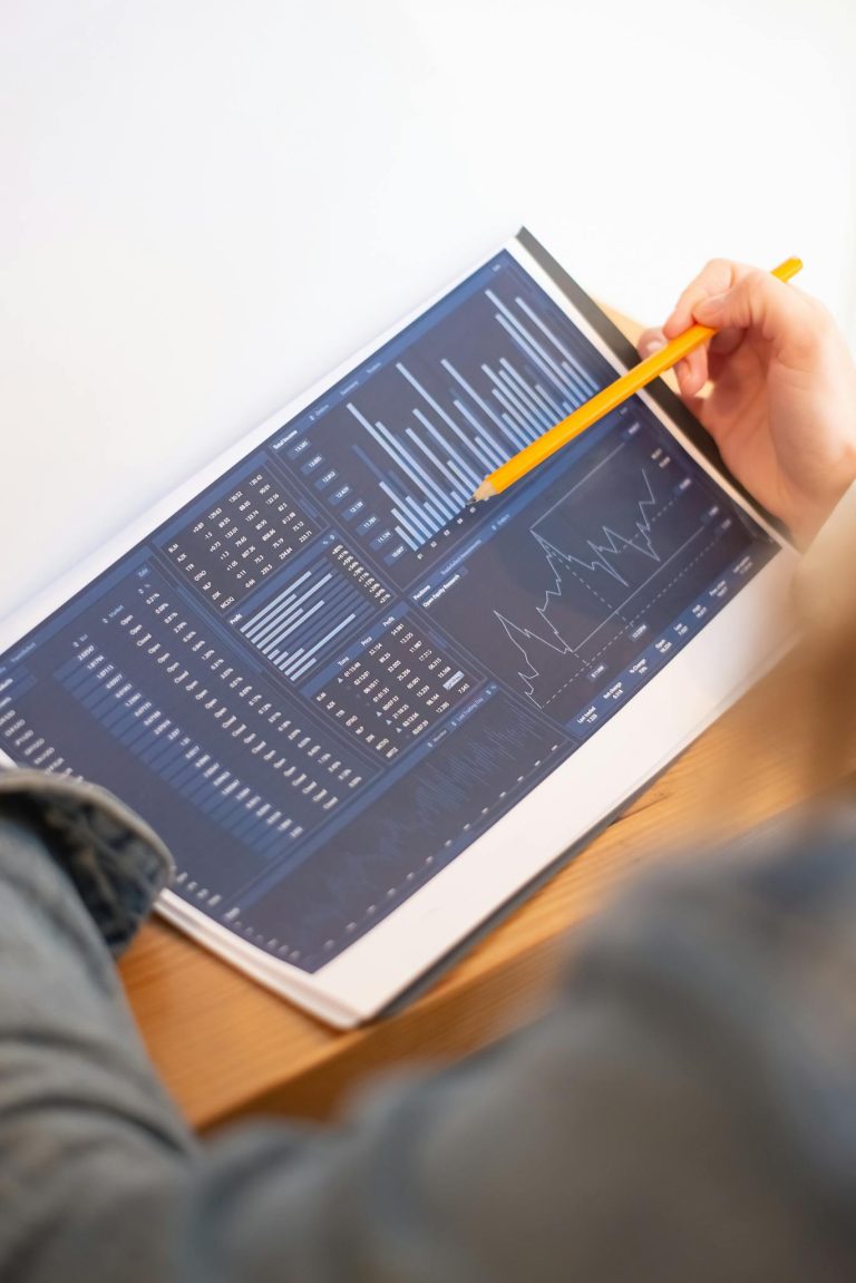 A close-up of a person analyzing blue graph data with a yellow pencil.